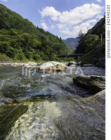 夏日美景:清澈的溪流潺潺流淌,翠綠的山巒在藍天白雲的映襯下熠熠生輝。 夏日美景:清澈的溪流潺潺流淌,翠綠的山巒在藍天白雲的映襯下熠熠生輝。 142448185