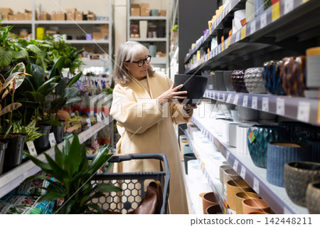 Mature woman shopping for ceramic flowerpot and plants in a retail store Mature woman shopping for ceramic flowerpot and plants in a retail store 142448211