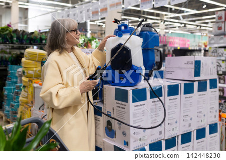 Senior woman shopping for a battery sprayer in a home improvement store Senior woman shopping for a battery sprayer in a home improvement store 142448230