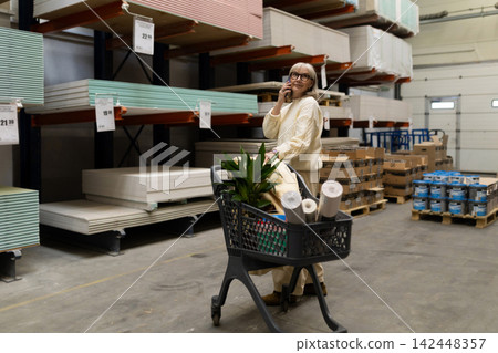 Mature woman talking on phone while pushing a shopping cart in a hardware store 142448357