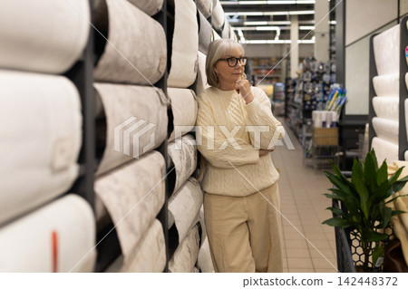 Mature woman leaning on wallpaper rolls, thoughtfully deciding on home decor 142448372