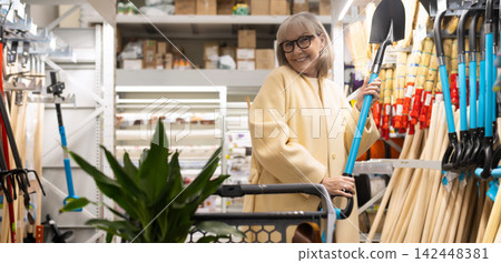 Smiling senior woman choosing a shovel in a hardware store aisle Smiling senior woman choosing a shovel in a hardware store aisle 142448381