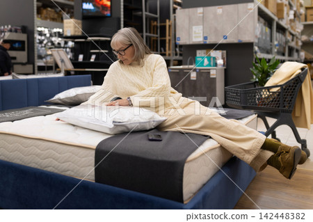 Mature woman trying a mattress in a department store, seeking comfort and quality Mature woman trying a mattress in a department store, seeking comfort and quality 142448382