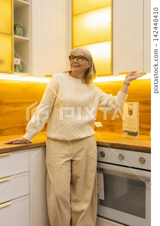 Senior woman in glasses enjoying a modern kitchen interior with new appliances 142448410