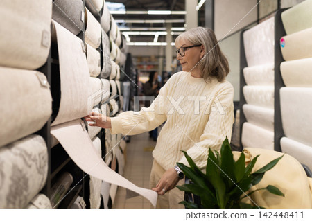 Mature woman shopping for wallpaper, renovating home interior design Mature woman shopping for wallpaper, renovating home interior design 142448411