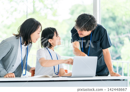 Male and female medical staff members are seen smiling and having a meeting around a computer. Male and female medical staff members are seen smiling and having a meeting around a computer. 142448667