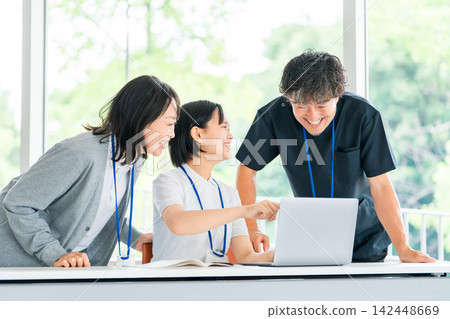 Male and female medical staff members are seen smiling and having a meeting around a computer. Male and female medical staff members are seen smiling and having a meeting around a computer. 142448669