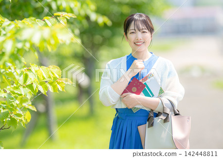 一位面帶微笑的女子手持護照,緊握著拳頭。 一位面帶微笑的女子手持護照,緊握著拳頭。 142448811