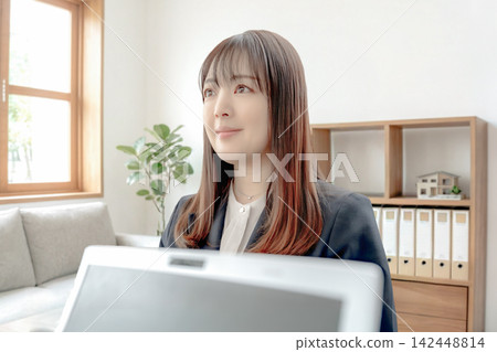 A woman smiles as she opens her laptop in a room with a model house. A woman smiles as she opens her laptop in a room with a model house. 142448814