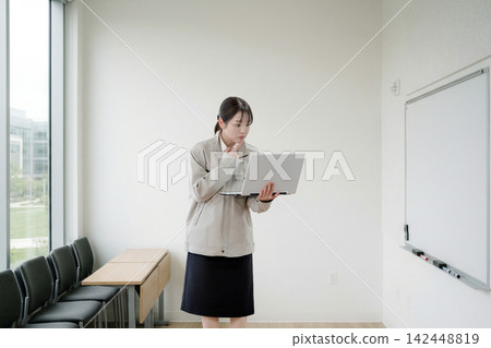 一位女士在會議室裡一邊看著筆記型電腦一邊思考。 142448819