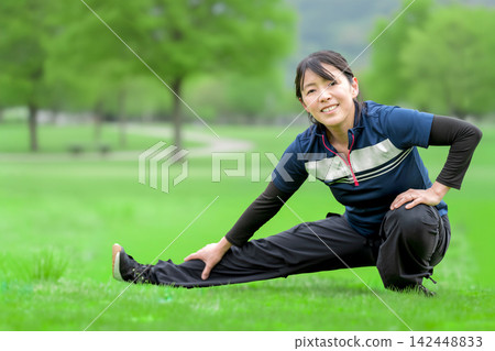 一位微笑的女子在綠草茵茵的公園裡伸展身體。 一位微笑的女子在綠草茵茵的公園裡伸展身體。 142448833