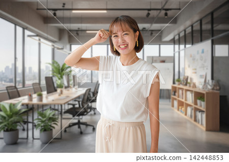 一位女士在時尚的辦公室裡擺出勝利的姿勢。 142448853