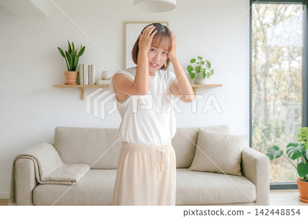 客廳裡,一位神情憂慮的女子雙手抱頭。 客廳裡,一位神情憂慮的女子雙手抱頭。 142448854