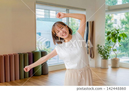 一位微笑的女子在瑜珈館高舉雙臂,活力四射地跳舞。 一位微笑的女子在瑜珈館高舉雙臂,活力四射地跳舞。 142448860