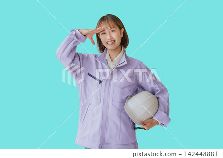 A woman in work clothes holds her hand to her forehead and gazes into the future against a light blue background. A woman in work clothes holds her hand to her forehead and gazes into the future against a light blue background. 142448881