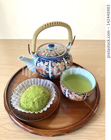 一個木製托盤上放著抹茶萩(裹著抹茶粉的年糕)、綠茶和一個圖案精美的茶壺。 一個木製托盤上放著抹茶萩(裹著抹茶粉的年糕)、綠茶和一個圖案精美的茶壺。 142448983