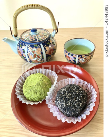 一組兩種口味的萩餅(年糕)——一種是抹茶口味,另一種是芝麻口味——盛放在紅色漆盤中,並配有綠茶茶壺。 一組兩種口味的萩餅(年糕)——一種是抹茶口味,另一種是芝麻口味——盛放在紅色漆盤中,並配有綠茶茶壺。 142448985