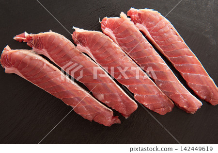Fresh raw tuna fillets arranged neatly on a dark slate surface, showcasing the vibrant pink color and texture of the fish meat Fresh raw tuna fillets arranged neatly on a dark slate surface, showcasing the vibrant pink color and texture of the fish meat 142449619