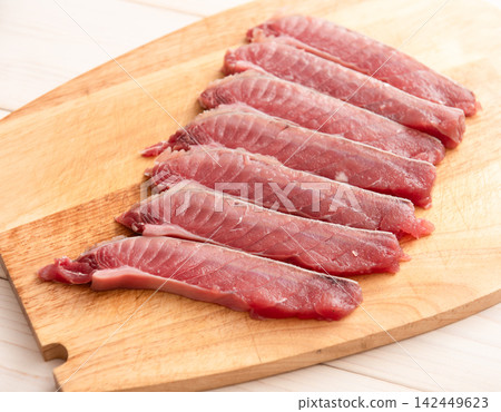 Fresh slices of raw fish arranged neatly on a wooden cutting board, showcasing the vibrant pink color and texture of the fish fillets Fresh slices of raw fish arranged neatly on a wooden cutting board, showcasing the vibrant pink color and texture of the fish fillets 142449623
