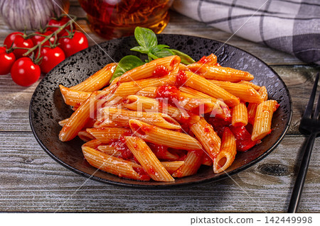 Penne pasta with tomato sauce on rustic plate with basil and cherry tomatoes 142449998