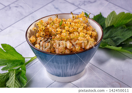 White currants in blue ceramic bowl with green leaves on marble surface White currants in blue ceramic bowl with green leaves on marble surface 142450011