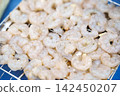 Raw peeled shrimps on a metal barbecue grill rack. 142450207