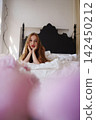 Redhead woman poses playfully on white bed in bright bedroom 142450212
