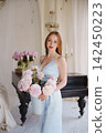 Woman in light blue dress holding peonies by piano 142450223