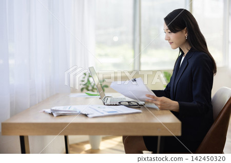 A young Japanese businesswoman working on her laptop by a bright window. A young Japanese businesswoman working on her laptop by a bright window. 142450320