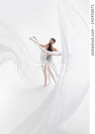 Graceful ballet couple reaches upward beneath flowing white fabric Graceful ballet couple reaches upward beneath flowing white fabric 142450671