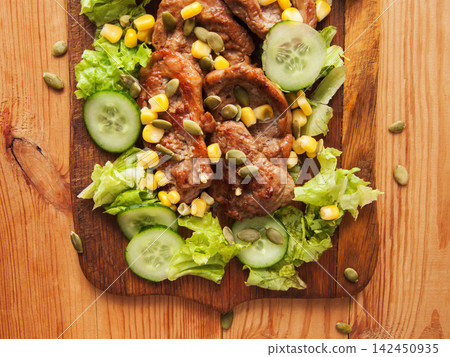 Juicy fried pork tenderloin steaks with sweet corn, green lettuce cucumbers salad. 142450935