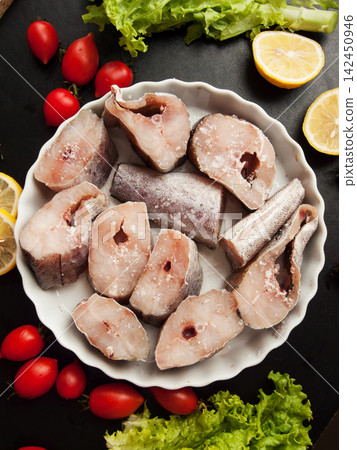 Fresh pollock seafood steaks with lettuce and cherry tomatoes seasoned with salt and lemon in pan Fresh pollock seafood steaks with lettuce and cherry tomatoes seasoned with salt and lemon in pan 142450946