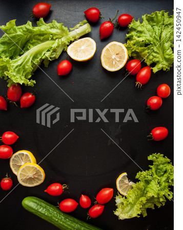 Frame made of red ripe fresh cherry tomatoes, green lettuce and cucumber on black background 142450947