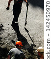 Unrecognizable road construction crew repairing asphalt street with shovels during maintenance 142450970