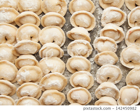 Raw homemade handmade russian pelmeni dumplings rows sprinkled with flour on metal tray Raw homemade handmade russian pelmeni dumplings rows sprinkled with flour on metal tray 142450982