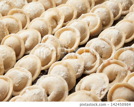 Raw homemade handmade russian pelmeni dumplings rows sprinkled with flour on metal tray Raw homemade handmade russian pelmeni dumplings rows sprinkled with flour on metal tray 142450984