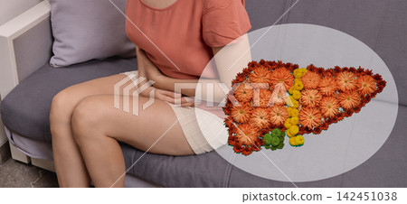 Woman sitting on a couch holding her aching stomach next to a floral liver illustration. Toxic hepatitis treatment, fatty liver, and cirrhosis diagnostics Woman sitting on a couch holding her aching stomach next to a floral liver illustration. Toxic hepatitis treatment, fatty liver, and cirrhosis diagnostics 142451038