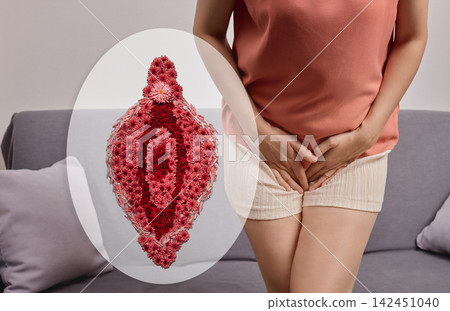 Woman sitting on a sofa holding her pelvic area next to a floral vulva illustration. Female intimate flora balance and reproductive wellness concept 142451040