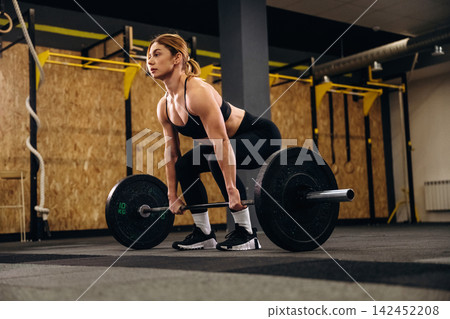 Female athlete performing deadlift exercise with barbell in modern gym, showcasing strength and focus in a well-equipped fitness environment 142452208