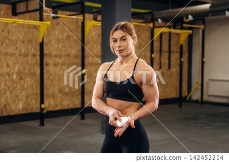 Female athlete applying chalk to hands in a gym setting, showcasing strength and preparation for weightlifting with equipment visible in the background Female athlete applying chalk to hands in a gym setting, showcasing strength and preparation for weightlifting with equipment visible in the background 142452214