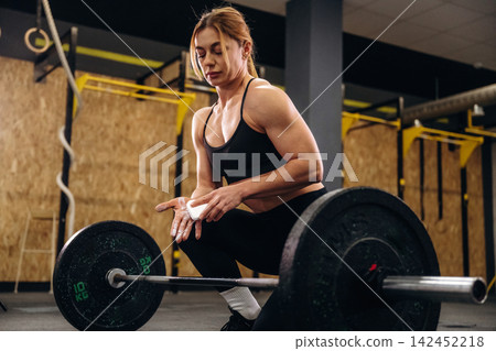 Female weightlifter in black sportswear prepares to lift a barbell with weights in a gym setting, focused on her technique and form during training Female weightlifter in black sportswear prepares to lift a barbell with weights in a gym setting, focused on her technique and form during training 142452218