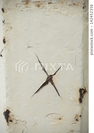 Peeling white paint covering a metallic surface, revealing rust and cracks forming a cross Peeling white paint covering a metallic surface, revealing rust and cracks forming a cross 142452356