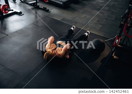 Female athlete performing push-ups on gym floor with fitness equipment and weights in the background, emphasizing strength training and workout routine Female athlete performing push-ups on gym floor with fitness equipment and weights in the background, emphasizing strength training and workout routine 142452461