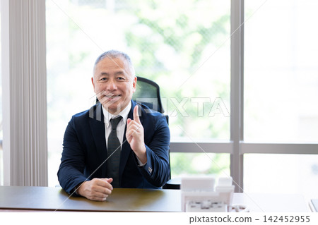 辦公室裡的一位資深商務人士一邊解釋某個觀點,一邊舉起食指微笑。 辦公室裡的一位資深商務人士一邊解釋某個觀點,一邊舉起食指微笑。 142452955