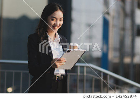 Business woman checks phone in front of modern building during the day Business woman checks phone in front of modern building during the day 142452974