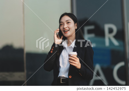 Business woman checks phone in front of modern building during the day Business woman checks phone in front of modern building during the day 142452975