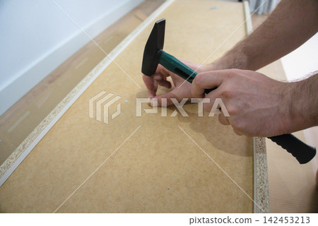 Man sets a nail and holds the hammer ready over a hardboard back Man sets a nail and holds the hammer ready over a hardboard back 142453213