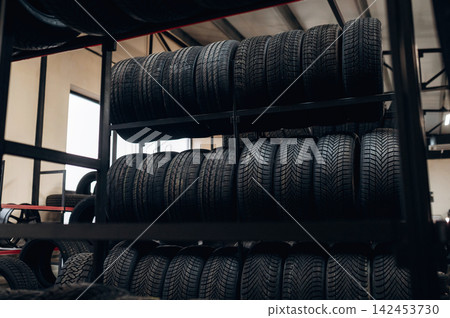Stack of black rubber tires neatly arranged on metal shelving inside an automotive workshop with natural light streaming through large windows Stack of black rubber tires neatly arranged on metal shelving inside an automotive workshop with natural light streaming through large windows 142453730