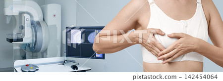 Woman touching her breast in a medical top near a modern mammography machine and display screen. Breast cancer screening, tumor detection, and mammogram diagnosis Woman touching her breast in a medical top near a modern mammography machine and display screen. Breast cancer screening, tumor detection, and mammogram diagnosis 142454064