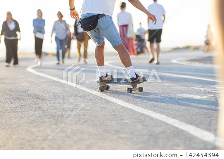 Skateboarding on a path as people walk by during the day at a busy outdoor area 142454394